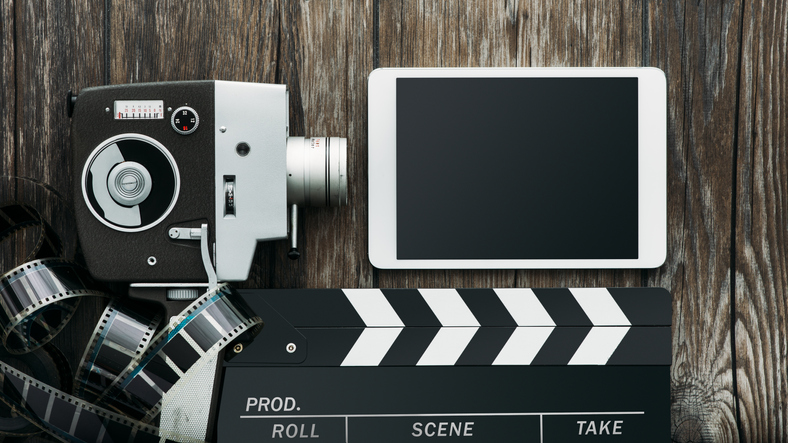 Vintage film camera, tablet, clapper and filmstrip on a wooden table: cinema and entertainment concept