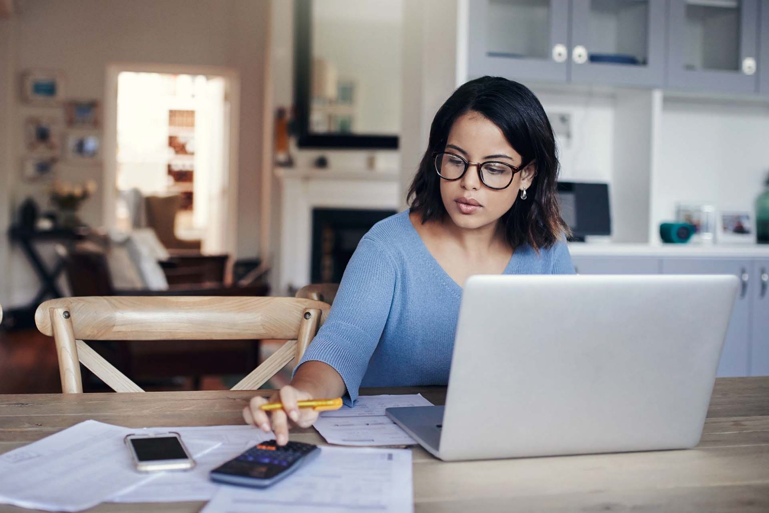 Shot of a young woman using a laptop and calculator while working from home