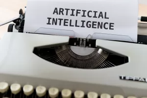 Photograph of a typewriter with a piece of paper fed through it displaying the words Artificial Intelligence.